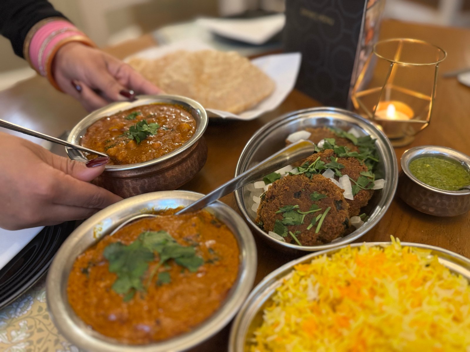 A shared table at Abbasi’s — curries in copper bowls, seekh kebab, biryani and poppadoms by candlelight